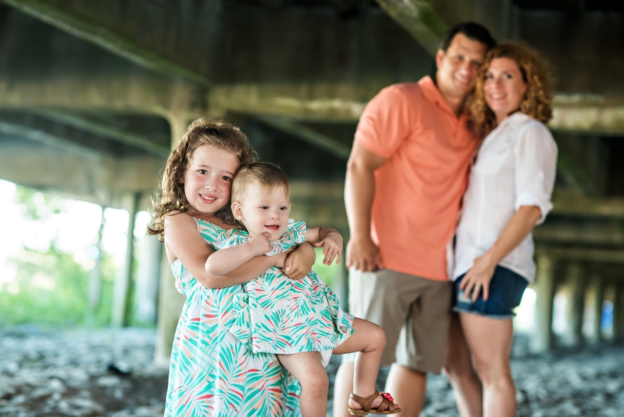 Parents watch as their daughters hug in a cute portrait under the boardwalk in Wildwood, NJ.